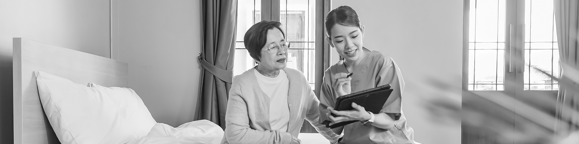 Woman sitting on a bed with a nurse who is reading questions from a tablet